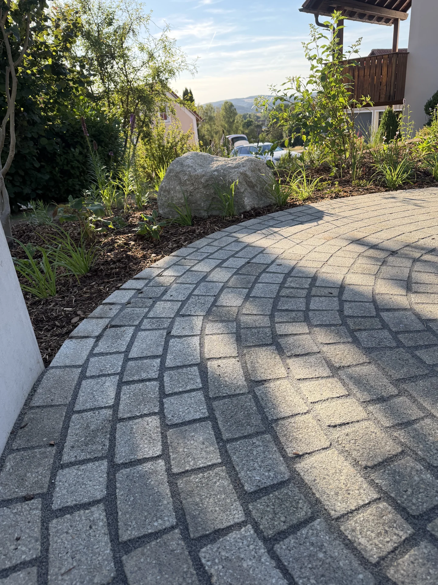 Geschwungener Pflasterweg mit bepflanzten Gartenbereichen
