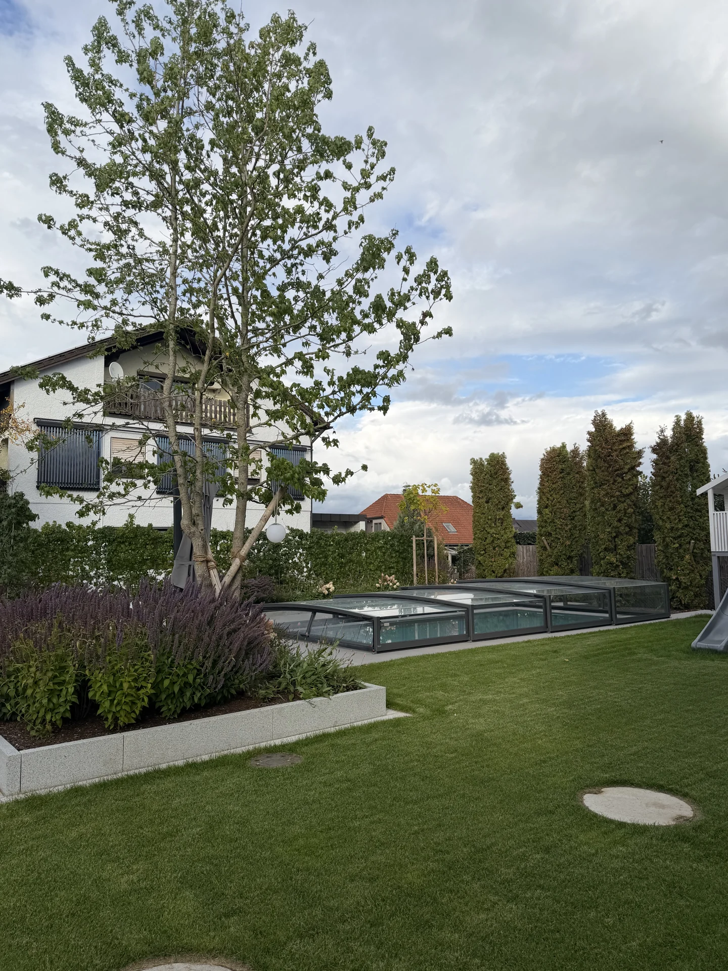 Gestaltetes Poolumfeld mit Poolüberdachung, Rasen und eingefasstem Pflanzbeet